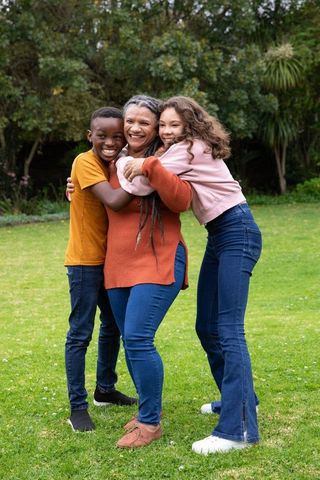 Happy Grandmother Hugging Grandchildren on Green Lawn