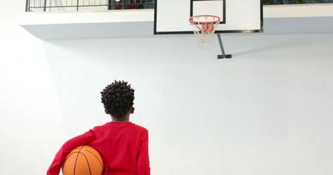 Young Boy Holding Basketball in Gym Looking at Hoop
