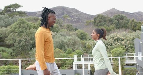 Indian woman and african american man stretching on modern terrace during outdoor workout