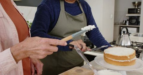 Senior women decorating sponge cake in modern kitchen