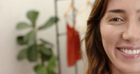 Confident woman smiling in boutique studio with clothing rack, green plant and soft bokeh