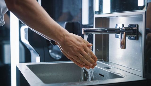 Male washing hands under chrome faucet in modern stainless sink with mirror reflections