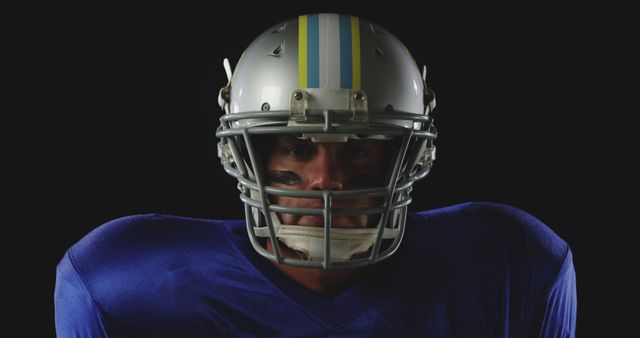 This image features a determined American football player wearing a helmet and blue jersey with face paint. Suitable for use in sports advertisements, articles about American football, or promotions for athletic gear.