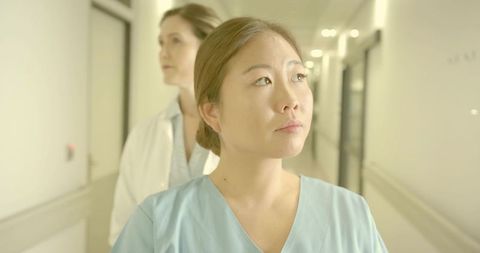 Nurse walking hospital corridor with doctor following, both looking forward