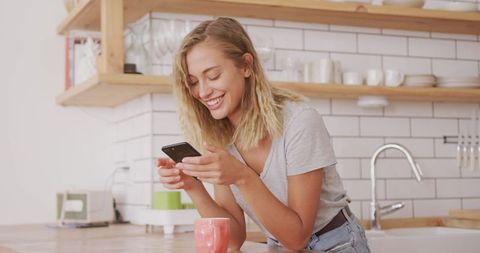 Smiling Woman Enjoying Smartphone in Cozy Kitchen