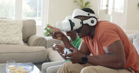 Father and son playing virtual reality games on living room couch with VR headsets