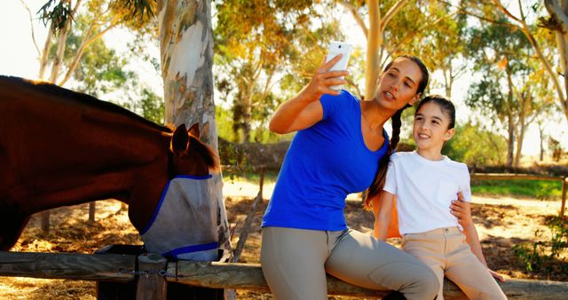 Parent and child capturing moment together while horse grazes nearby in rural outdoor environment. Great for themes related to family bonds, rural life, outdoor activities, animal interactions, summer days. Can be used for blog posts, advertisements, family-centered campaigns.