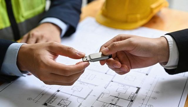 Construction team sharing usb drive over architectural blueprints during site meeting
