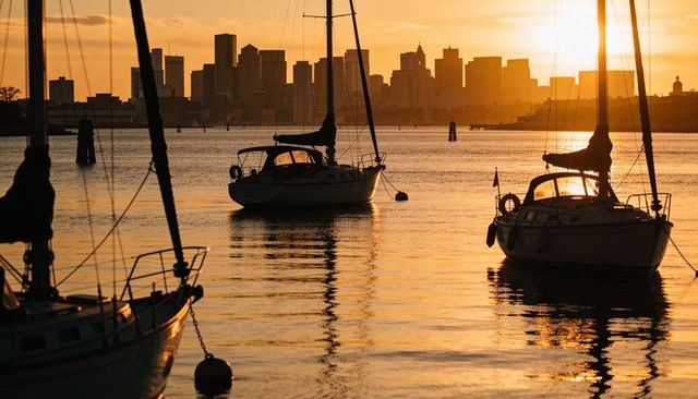 Golden sunset sailboats silhouetted against urban skyline with reflective water