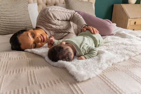 Mother bonding with newborn on cozy bed watching baby in sage green onesie