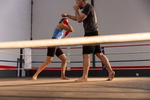 Female boxer sparring barefoot with male coach in boxing ring training session with red gloves