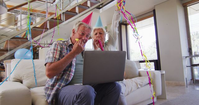 Elderly couple sitting on couch, engaging in virtual party with laptop. Wearing colorful party hats, surrounded by a festive atmosphere. Ideal for themes related to socially distant celebrations, senior lifestyle, digital connectedness, and joyful moments.