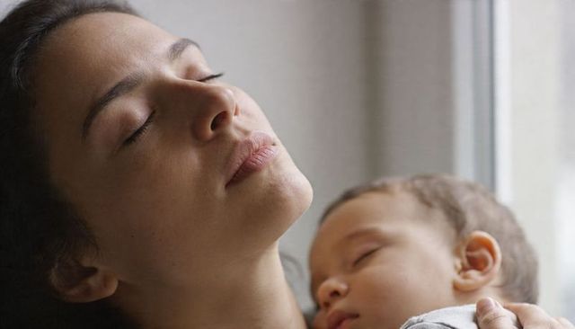 Cradling mother holding sleeping infant near window showing tender bonding and serene moment