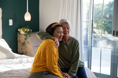 Senior women embracing on bed sharing comfort and affection in sunlit home interior