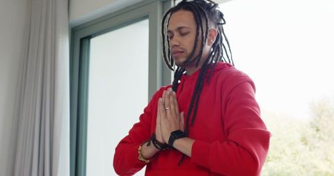 Young man meditating with hands in prayer wearing red hoodie and smartwatch