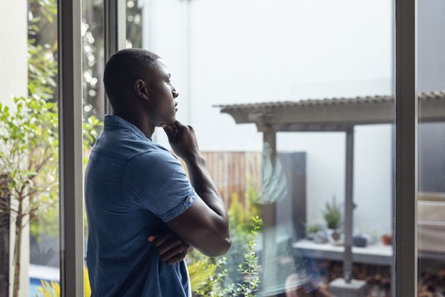 Side view of african american thoughtful mid adult man with hand on chin looking through window - Download Free Stock Photos Pikwizard.com