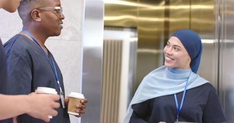 Medical staff sharing coffee and smiling during elevator break in hospital corridor