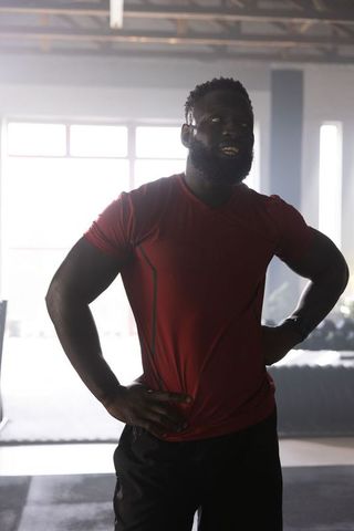Backlit african american athlete standing in industrial gym wearing red shirt post-training