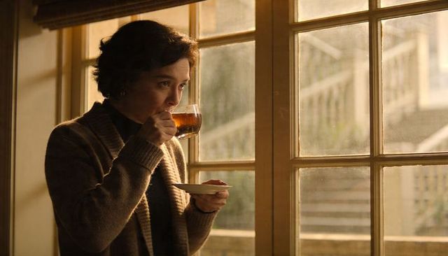 Middle-aged woman sipping tea in cozy brown cardigan by sunlit wooden window, soft morning light