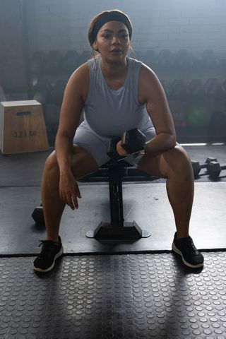 Focused african american woman resting with dumbbell on bench in urban gym moody lighting