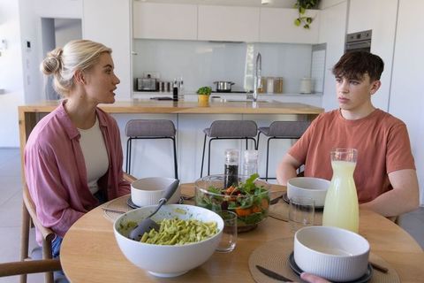 Mother and teen son having serious conversation at modern kitchen dining table
