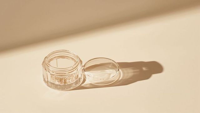 Transparent cosmetic jar on beige surface with warm shadows