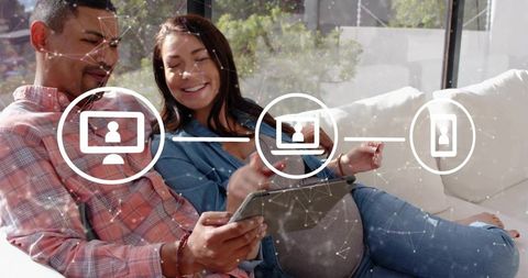 Midadult couple using tablet on sofa, sharing digital content with networked device icons