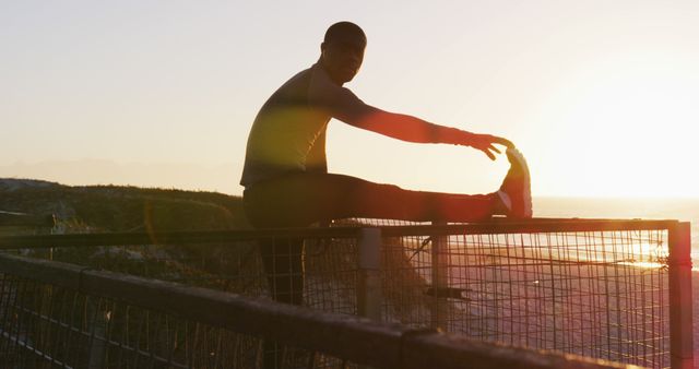 Focused african american man stretching, exercising outdoors by seaside at sunset. fitness, healthy and active lifestyle concept.