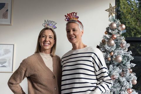 Women smiling and posing in festive merry christmas headbands by frosted holiday tree