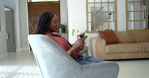 African american woman relaxing in modern living room sitting on armchair using smartphone