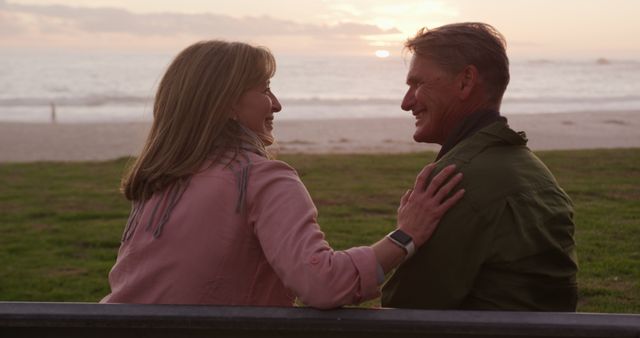 Happy senior couple sitting on bench by beach during sunset, enjoying romantic moment together. Perfect for advertisements about love, relationships, retirement, or travel.