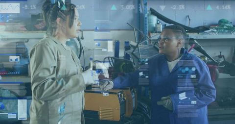 Mechanics discussing diagnostic HUD while adjusting orange battery charger in workshop