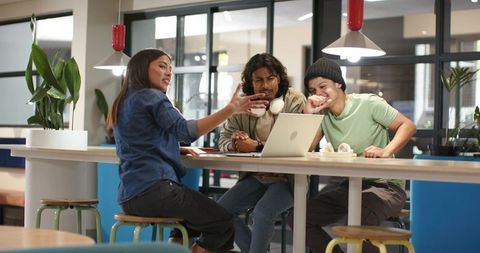 Young diverse team collaborating around laptop in modern coworking lounge