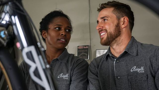 Bike shop technicians chatting while servicing bicycle, teamwork and workshop maintenance