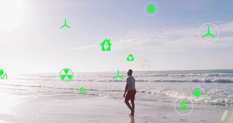 Walking mature man on sunlit beach surrounded by floating green renewable energy icons