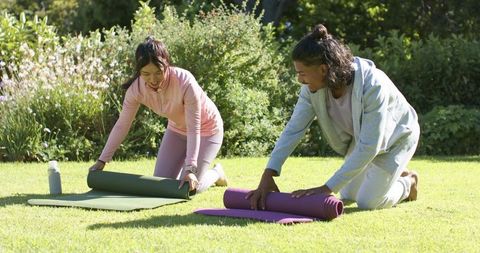 Couple unrolling yoga mats on sunlit backyard lawn practicing mindful outdoor fitness