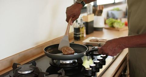 Chef Flipping Burger Patties on Stove in Modern Kitchen