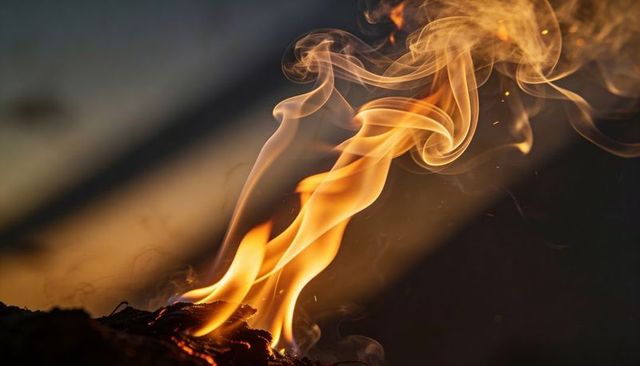 Flickering flame curling smoke over glowing embers close-up for dramatic background