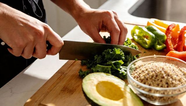 Chopping kale with avocado and quinoa on wooden cutting board for healthy meal prep