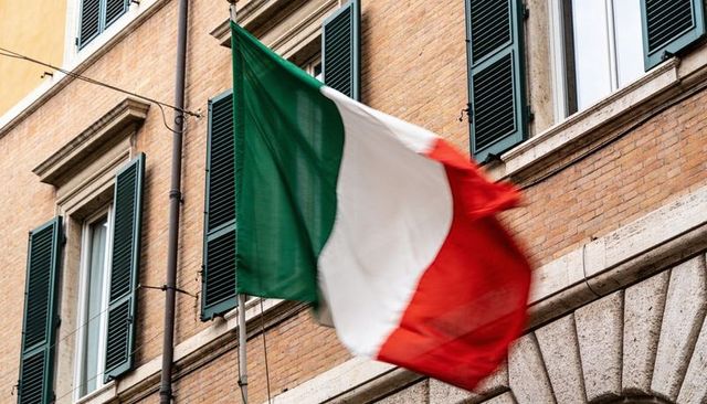 Italian flag waving from brick facade with green shutters and motion blur