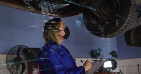 Female automotive technician inspecting lifted wheel with digital diagnostics and clipboard