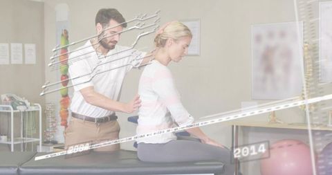 Physical therapist assessing spinal posture of female patient on treatment table, anatomy charts