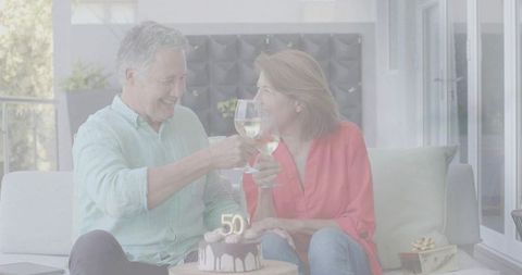 Mature Couple Toasting and Celebrating 50th Anniversary with Wine and Cake on Cozy Sofa