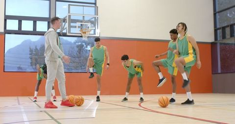 Basketball coach leading warm-up with diverse team on indoor court