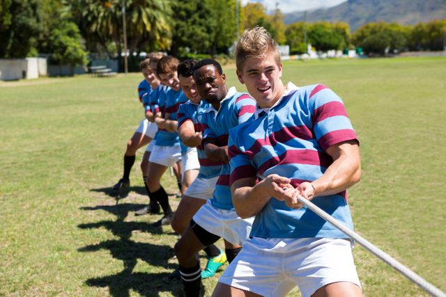 Rugby players palying tug of war while standing on grassy field against sky