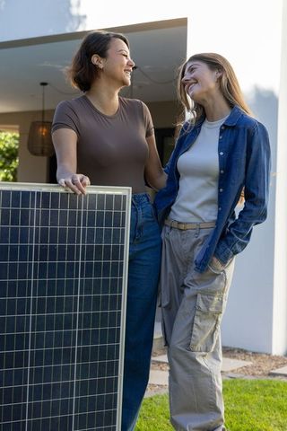 Smiling friends standing by solar panel in backyard promoting sustainable home energy