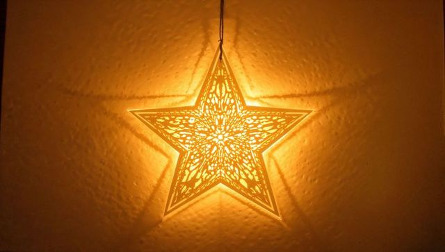 Glowing star lantern casting intricate radial shadows on textured wall, warm ambient light