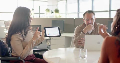 Diverse team presenting tablet chart during collaborative meeting in modern office