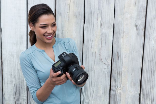Happy female photographer standing against wooden background