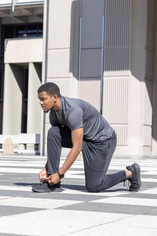 African american man tying running shoe on urban plaza preparing for sunny outdoor workout